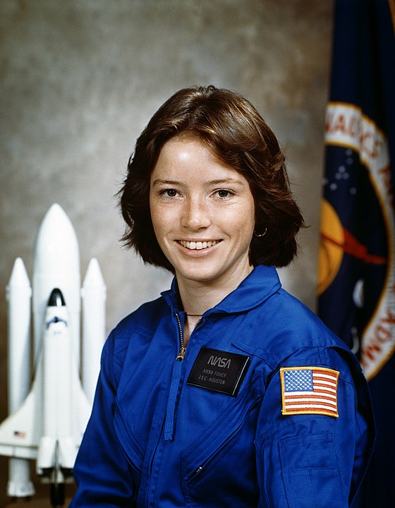 Anna Fisher is a Whte woman. She is smiling in a blue NASA uniform